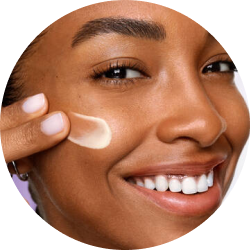 Lächelnde Frau trägt die Lancôme Rénergie SPF50 H.P.N. UVMUNE Cream mit einem Finger auf ihre Wange auf.